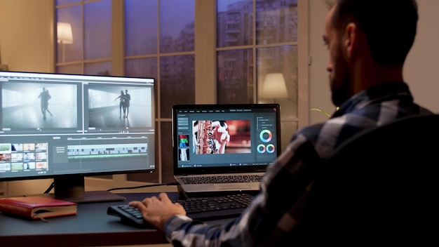 Vue arrière du créateur de contenu travaillant au bureau à domicile pendant la nuit. Éditeur vidéo dans le bureau à domicile.