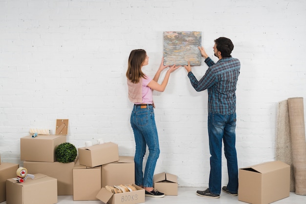 Vue arrière du jeune couple en plaçant un cadre photo sur un mur blanc avec des boîtes en carton