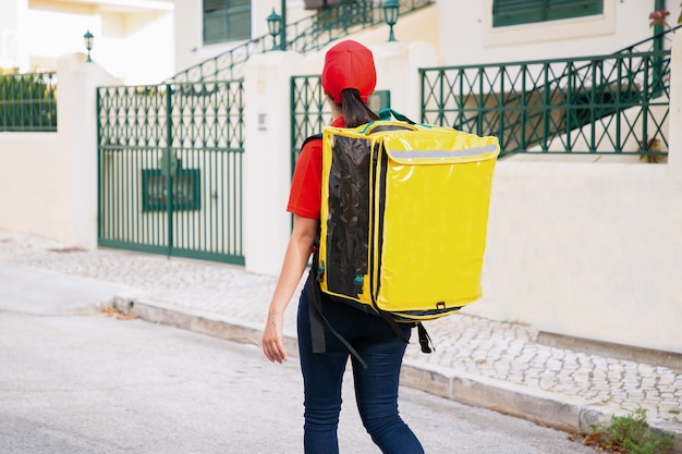 Photo gratuite vue arrière du livreur transportant un sac thermo jaune. courrier expérimenté marchant dans la rue à l'extérieur et livrant la commande.