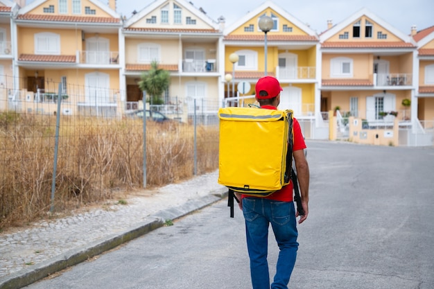 Vue arrière du livreur transportant un sac thermo jaune. Courrier professionnel marchant dans la rue et livrant la commande à pied.