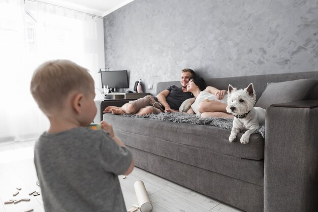 Vue arrière du petit garçon en regardant ses parents se détendre sur le canapé avec chien