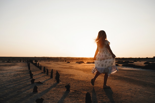 Vue arrière de l'enfant dansant sur le sable le soir avec coucher de soleil