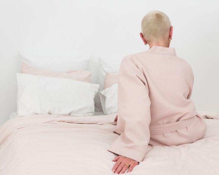 Photo gratuit vue arrière d'une femme âgée en peignoir assis sur un lit avec espace copie