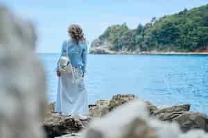Photo gratuite vue arrière d'une femme aux cheveux bouclés debout en robe bleue regardant vers la mer et le ciel bleus