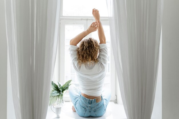 Vue arrière de la femme blonde aux cheveux bouclés se détendre à la maison