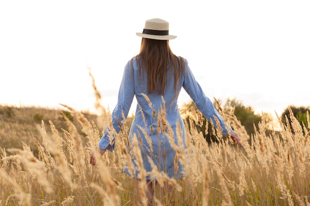 Photo gratuite vue arrière de la femme avec chapeau posant à travers les champs