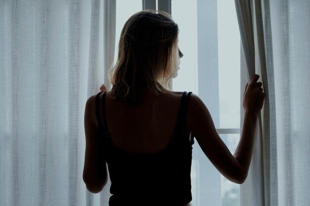 Vue arrière d'une femme debout près de la fenêtre