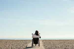 Photo gratuite vue arrière de la femme en fauteuil roulant à la plage