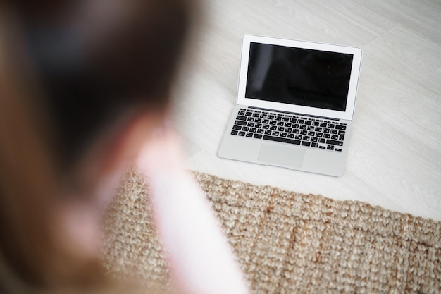Vue arrière de la femme en forme assise sur un tapis en regardant une vidéo sur un ordinateur portable