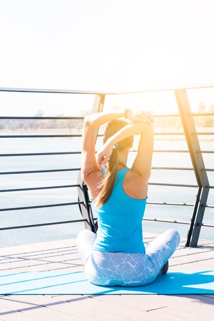 Vue arrière de la femme jeune de remise en forme qui s&#39;étend de sa main, assis sur un pont au soleil du matin