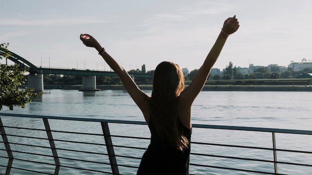 Vue arrière d&#39;une femme levant les bras devant la rivière