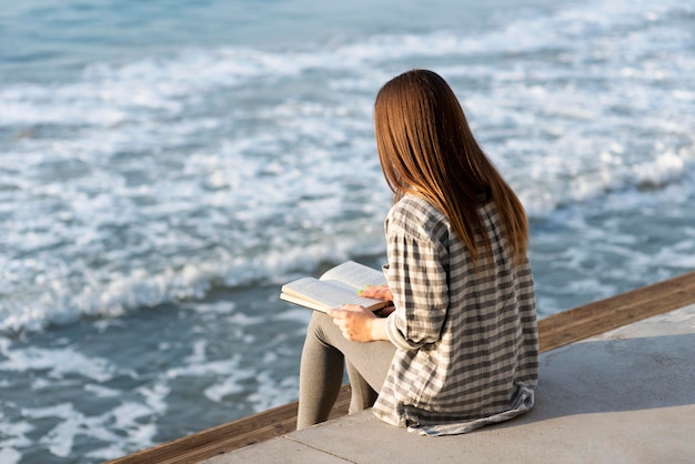 Vue arrière femme lisant à côté de la mer