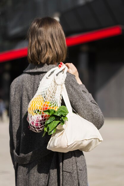 Vue arrière femme portant un sac écologique avec des légumes biologiques