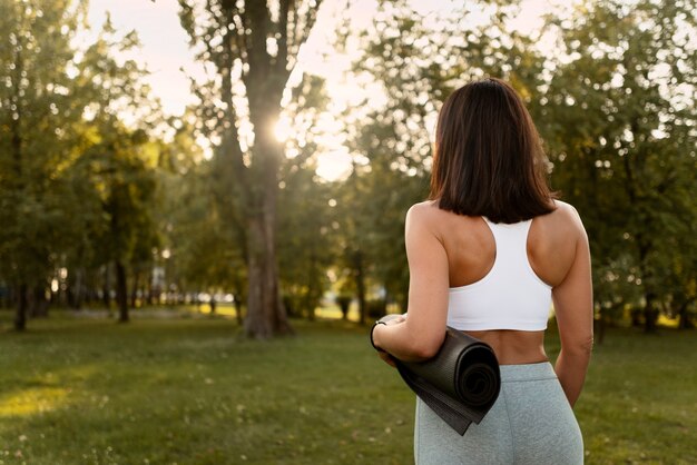 Photo gratuite vue arrière femme tenant un tapis de yoga