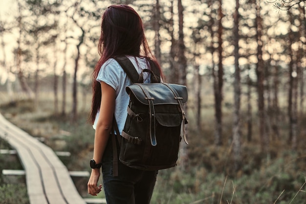 Vue arrière d'une fille touristique avec sac à dos à pied sur un sentier en bois dans une belle forêt.