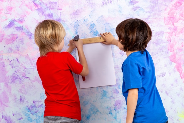 Vue arrière des garçons travaillant avec un marteau en t-shirts rouges et bleus sur un mur coloré