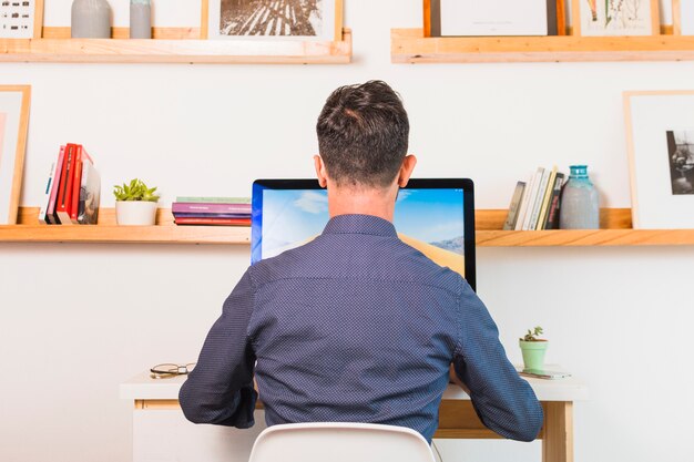 Vue arrière d&#39;un homme assis sur une chaise à l&#39;aide d&#39;un ordinateur de bureau