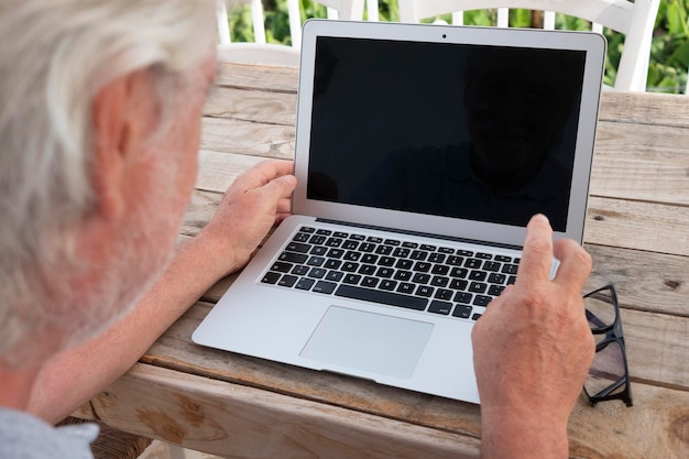 Vue arrière d'un homme barbu senior avec des cheveux blancs et des lunettes à l'aide d'un ordinateur portable en plein air