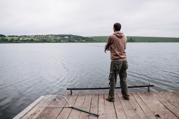 Photo gratuite vue arrière de l'homme debout sur la jetée de pêche dans le lac