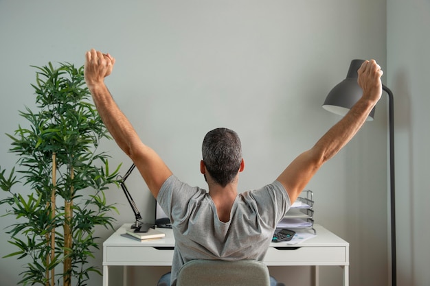 Vue arrière de l'homme étirant ses bras tout en travaillant à domicile