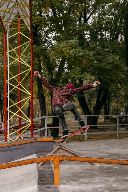 Vue arrière de l'homme faisant des tours avec skateboard à l'extérieur dans le parc