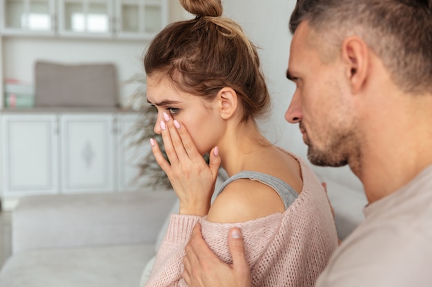 Vue arrière de l'homme prudent assis sur le canapé et calmer sa petite amie bouleversée qui pleure à la maison