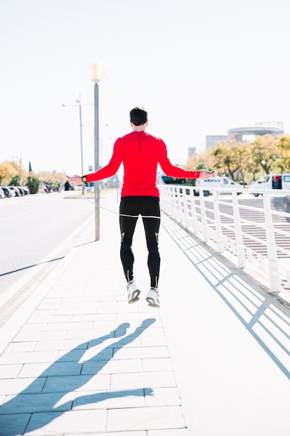 Vue arrière homme sautant à la corde sur le trottoir