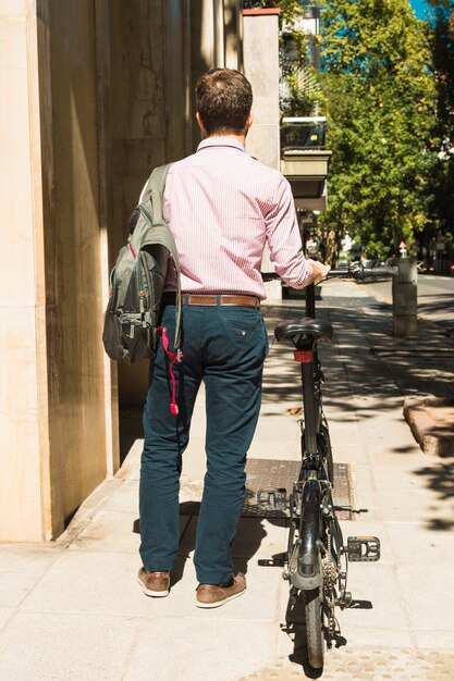 Vue arrière d&#39;un homme avec son sac à dos, marchant à vélo