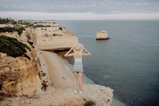 Vue arrière de la jeune femme au chapeau et jolie robe d'été debout sur la pierre