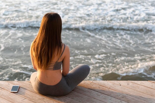 Vue arrière jeune femme méditant à côté de la mer