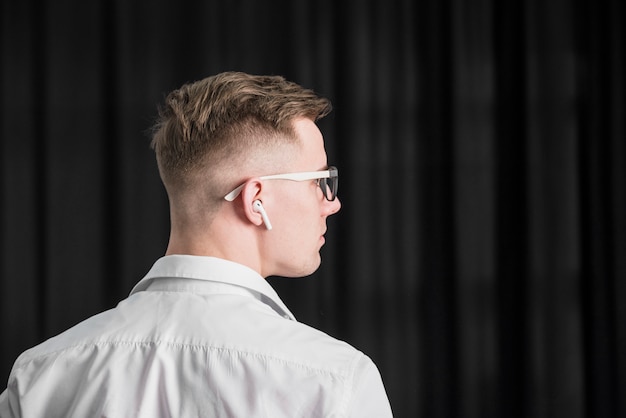 Vue arrière d&#39;un jeune homme portant des lunettes avec un écouteur sans fil sur son oreille