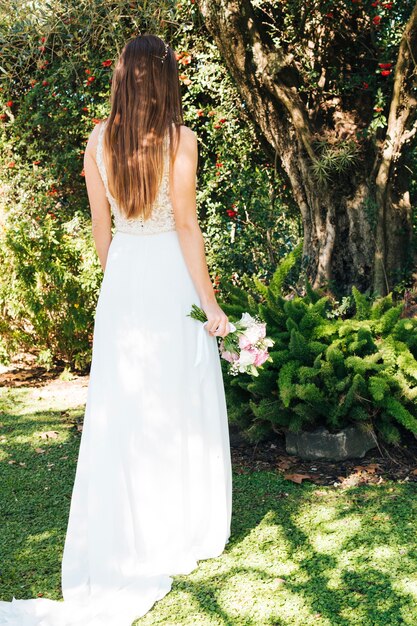 Vue arrière d&#39;une mariée tenant un bouquet de fleurs à la main, debout dans le parc