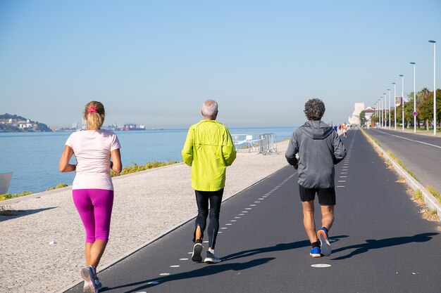 Vue arrière de personnes d'âge mûr portant des vêtements de sport, jogging le long de la rive du fleuve. Toute la longueur. Concept de retraite ou de mode de vie actif