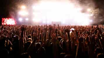 Photo gratuite vue arrière de personnes excitées avec les bras levés s'amusant tout en regardant des feux d'artifice de confettis devant la scène au festival de musique espace de copie