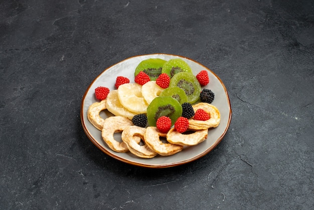 Vue avant des anneaux d'ananas séchés avec des kiwis et des pommes séchées sur la surface gris foncé fruits secs raisins secs bonbons de sucre sucré