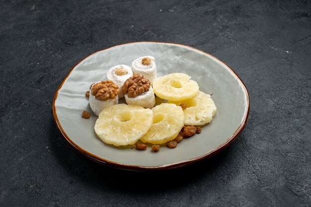 Vue avant des anneaux d'ananas séchés avec des raisins secs à l'intérieur de la plaque sur la surface grise fruits secs raisins secs sweet photo