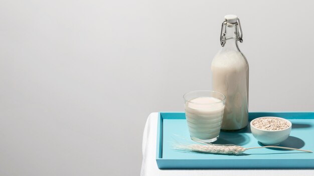 Vue avant de la bouteille de lait sur le plateau avec verre et flocons d'avoine