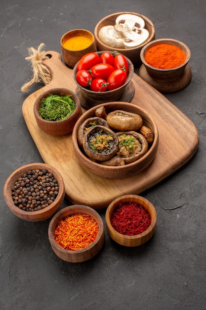 Vue avant de champignons cuits avec assaisonnements sur une table gris foncé des aliments mûrs sauvages