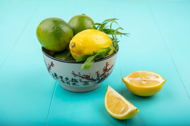 Vue avant des citrons sur un bol avec de l'estragon sur une surface bleue