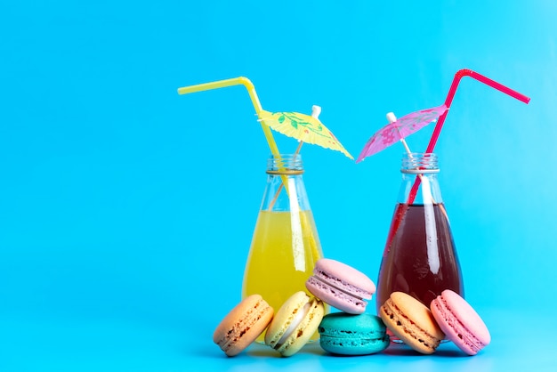 Photo gratuite une vue avant des cocktails colorés de refroidissement avec des pailles avec des macarons français sur bleu