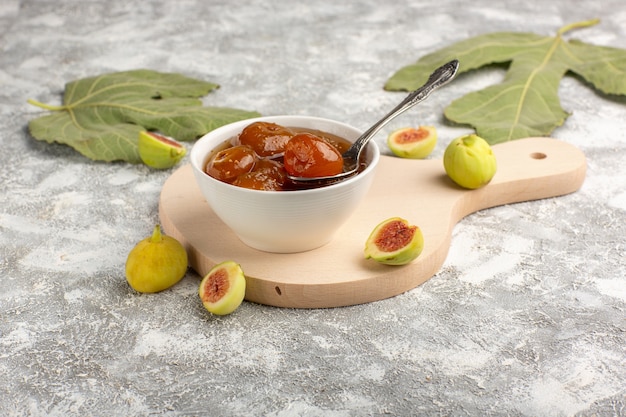 Vue avant de la confiture de figues sucrées avec des fleurs sur le sol blanc