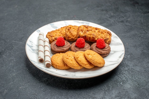 Vue avant des cookies et des gâteaux à l'intérieur de la plaque sur l'espace gris