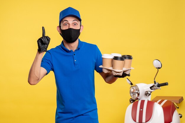 Vue avant de courrier masculin en masque noir tenant le café sur le travail jaune covid- service de travail uniforme de livraison pandémique