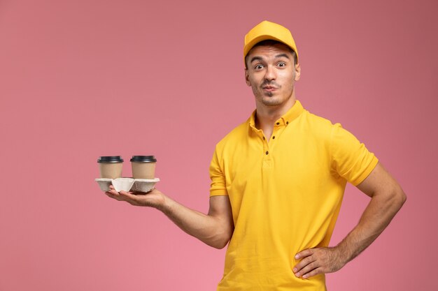 Vue avant de courrier masculin en uniforme jaune tenant des tasses de café de livraison sur le fond rose clair