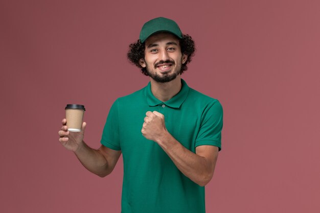 Vue avant de courrier masculin en uniforme vert et cape tenant la tasse de café de livraison sur le fond rose service de livraison uniforme travail travail entreprise masculine