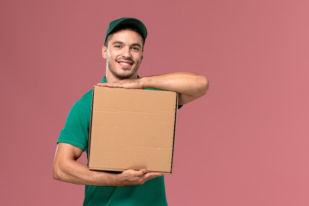 Vue avant de courrier masculin en uniforme vert tenant la boîte de nourriture avec le sourire sur le fond rose