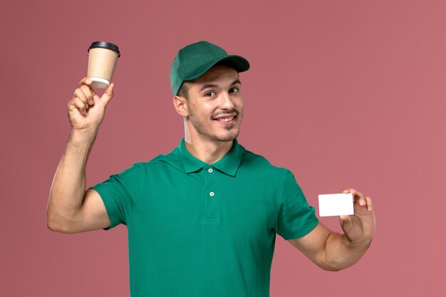 Vue avant de courrier masculin en uniforme vert tenant la tasse de café de livraison avec carte blanche sur rose clair