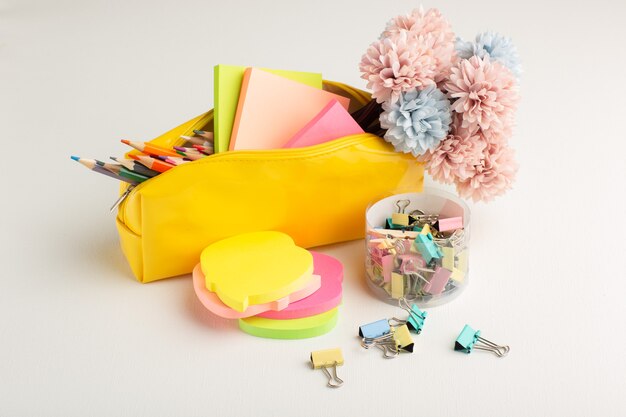 Vue avant des crayons colorés avec boîte à stylos et autocollants sur un bureau blanc