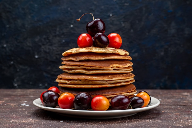 Une vue avant de délicieuses crêpes aux cerises à l'intérieur de la plaque blanche sur la crêpe aux fruits de bureau noir