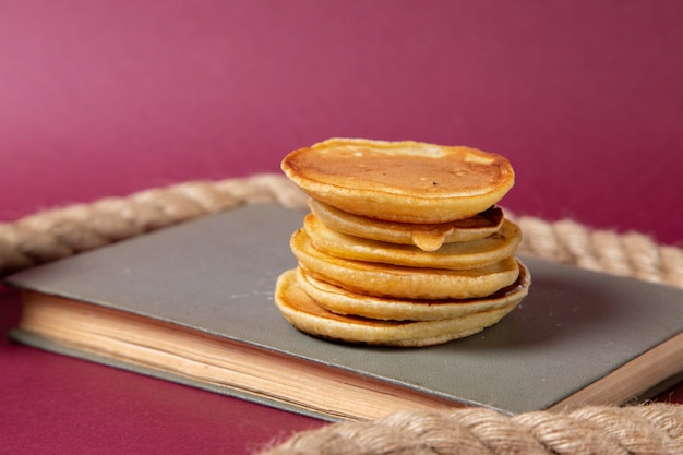 Vue avant de délicieuses crêpes cuites sur le cahier sur le fond rose de la nourriture pour le petit-déjeuner sucré